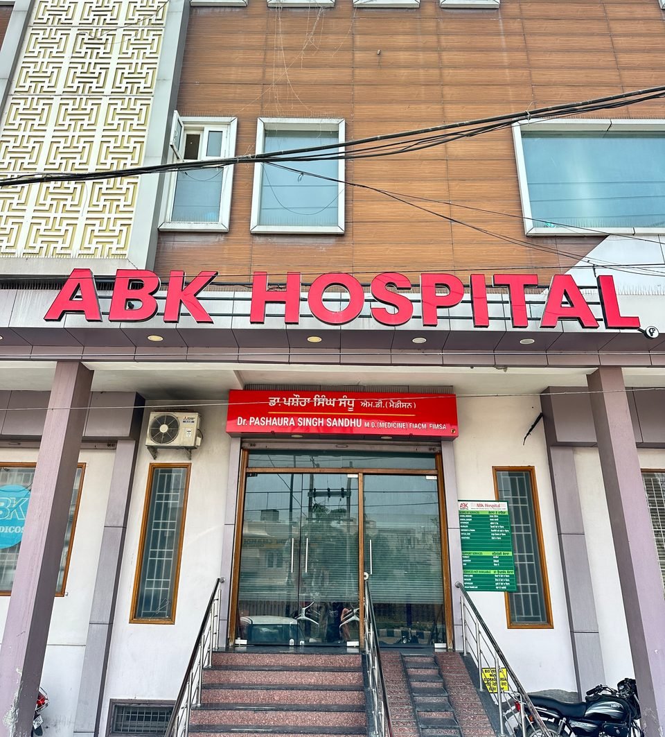 ABK Hospital's front: a red ABK HOSPITAL sign above glass doors, with steps and a handrail up to the entrance