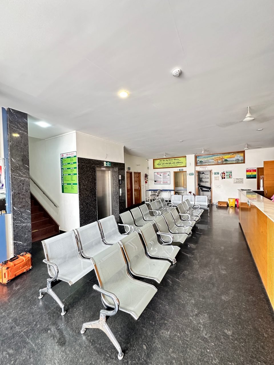 Rows of waiting chairs in a hall with a lift and a staircase